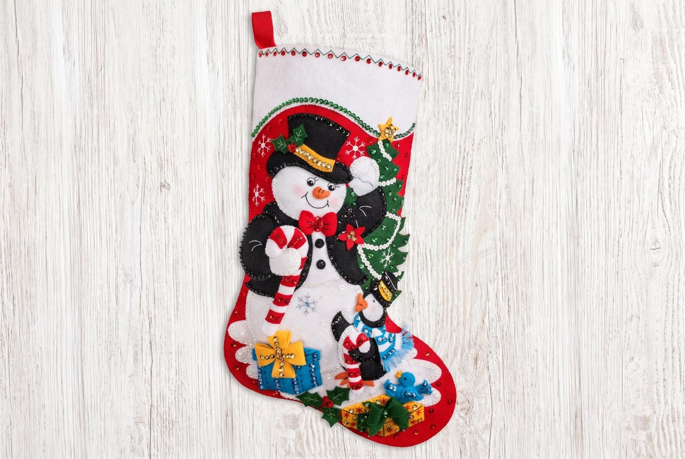Bucilla Dapper Snowman felt-applique stocking 89530E — deep red base with a bold white snowman in a black top hat and red bow tie, penguin, and candy cane