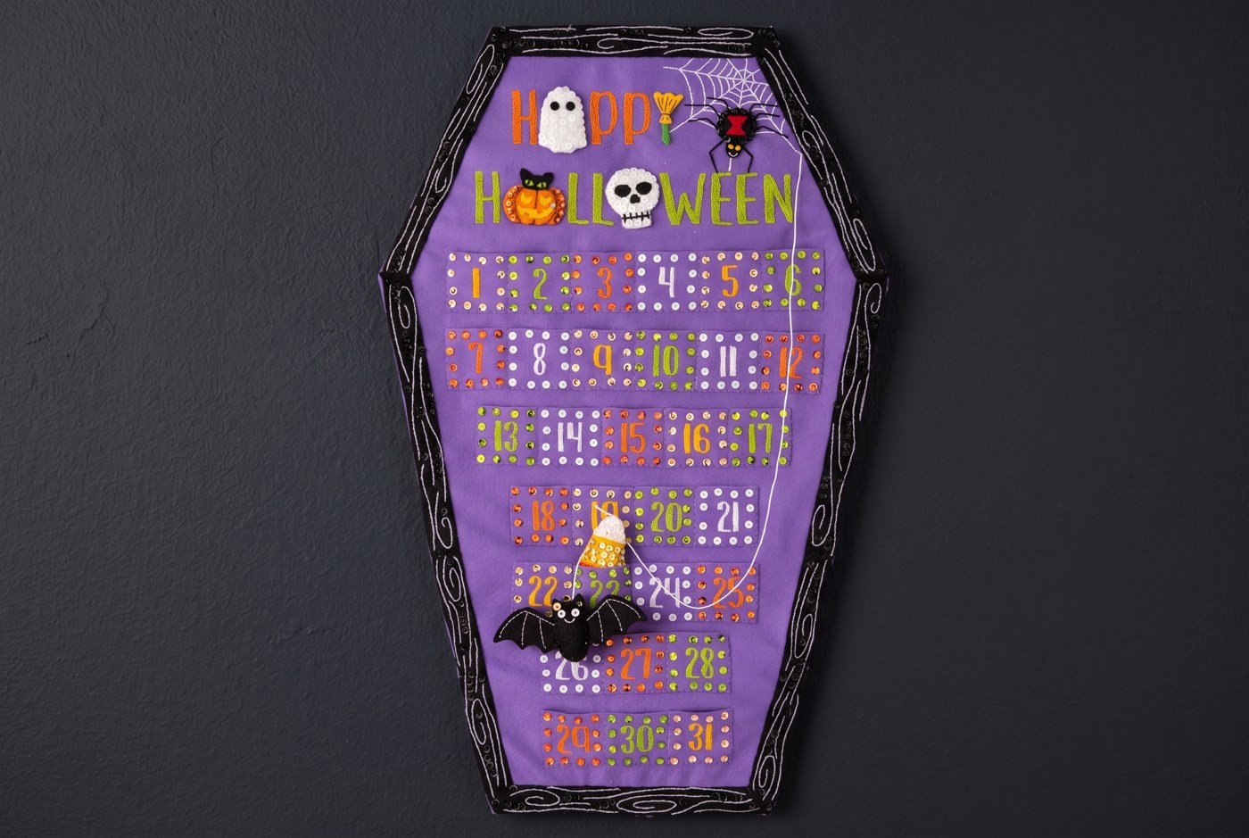 Bucilla Halloween Countdown wall hanging felt-applique kit (89728E) Halloween Countdown Calendar 89728E felt applique coffin-shaped wall hanging with numbers 1 through 31 on dark wall