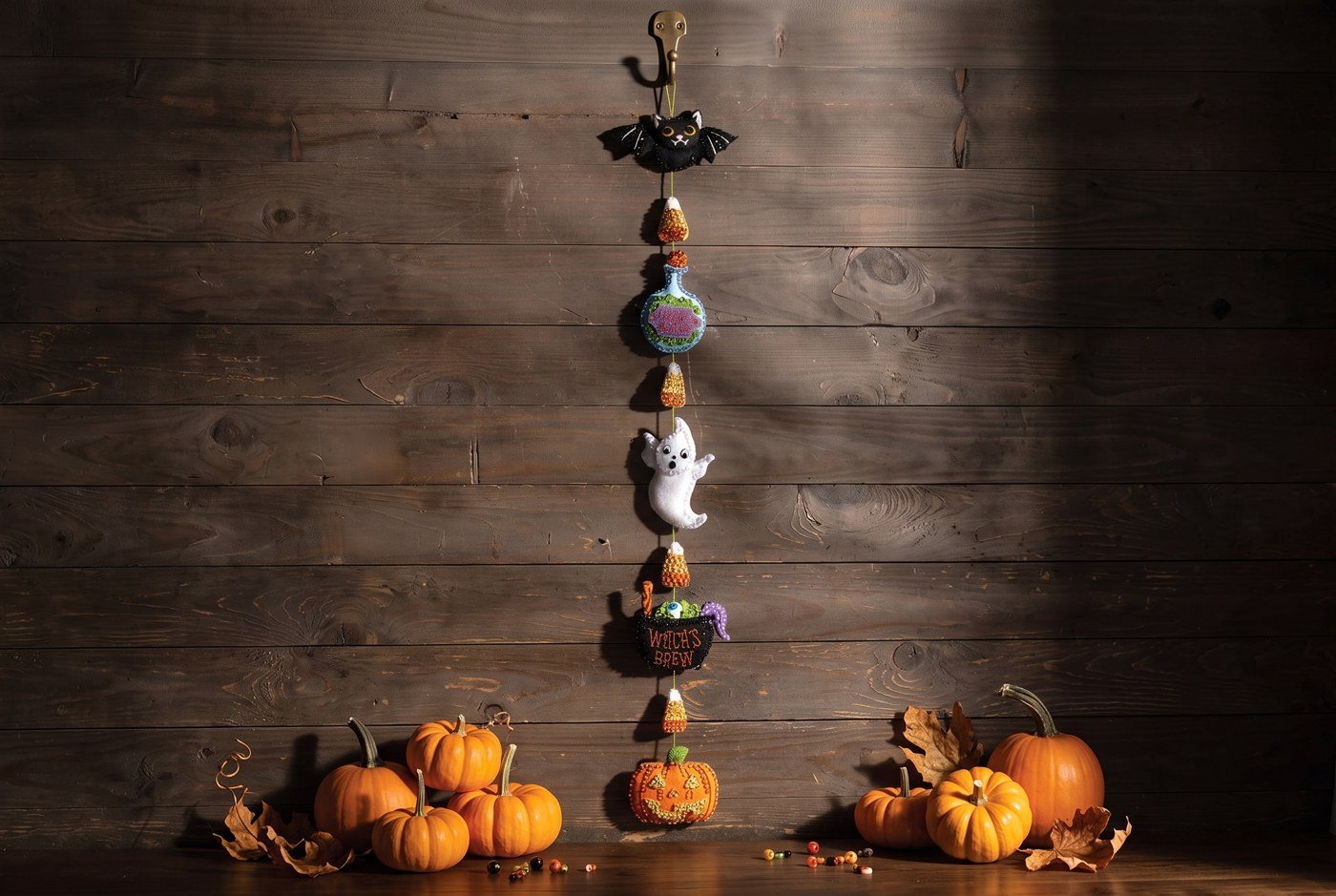 Bucilla Spells and Sweets Halloween felt-applique garland kit (89794E) Spells and Sweets Garland 89794E felt applique — vertical Halloween garland with bat ghost cauldron and jack-o-lantern on dark wood wall